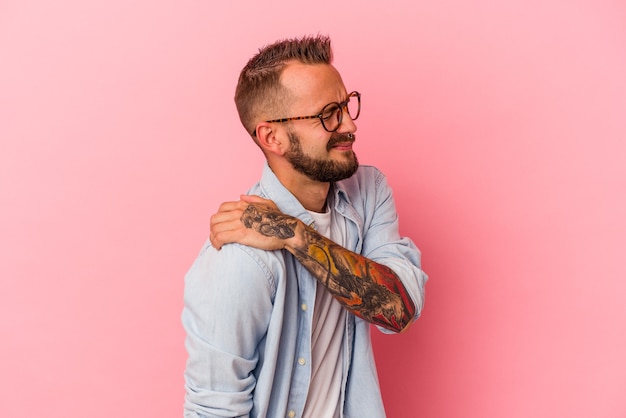 Jeune homme de race blanche avec des tatouages isolés sur fond rose ayant une douleur à l'épaule.