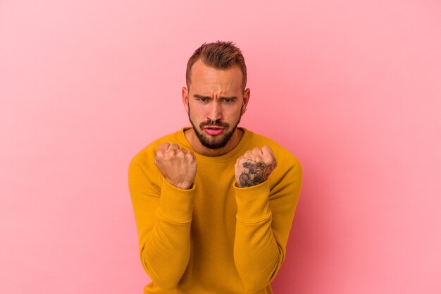 Jeune homme de race blanche avec des tatouages isolés sur fond rose contrarié en criant avec des mains tendues.