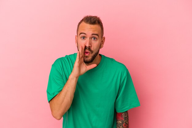 Un jeune homme de race blanche avec des tatouages isolés sur fond rose dit une nouvelle secrète de freinage à chaud et regarde de côté