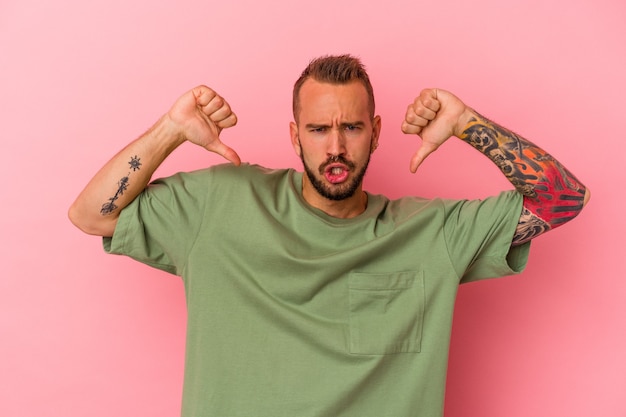 Jeune homme de race blanche avec des tatouages isolés sur fond rose se sent fier et confiant, exemple à suivre.