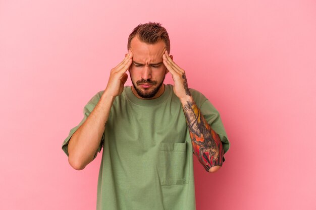 Jeune homme de race blanche avec des tatouages isolés sur fond rose touchant les temples et ayant des maux de tête.