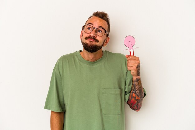 Jeune Homme De Race Blanche Avec Des Tatouages Tenant Une Sucette Isolée Sur Fond Blanc Rêvant D'atteindre Des Objectifs