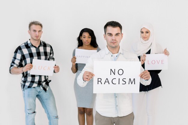 Jeune homme de race blanche tenant aucun signe de racisme, trois militants amis multiethniques tenant des slogans sociaux, amour, bonheur