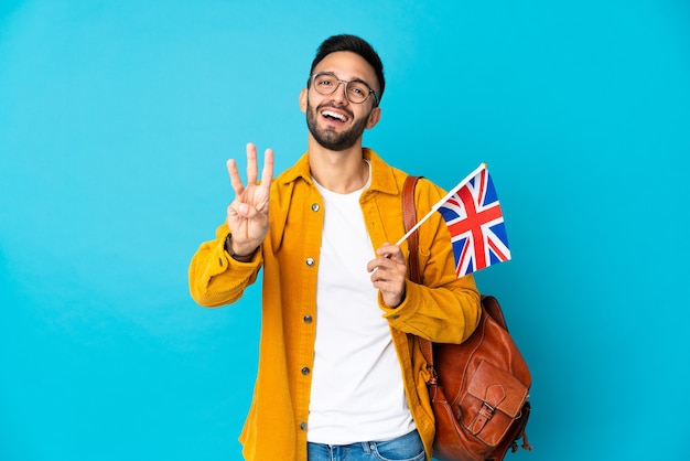 Jeune homme de race blanche tenant un drapeau du Royaume-Uni isolé sur fond jaune heureux et en comptant trois avec les doigts