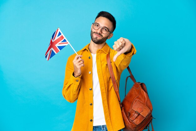 Jeune homme de race blanche tenant un drapeau du Royaume-Uni isolé sur fond jaune montrant le pouce vers le bas avec une expression négative