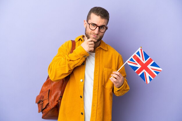 Jeune homme de race blanche tenant un drapeau du Royaume-Uni isolé sur fond violet pensant