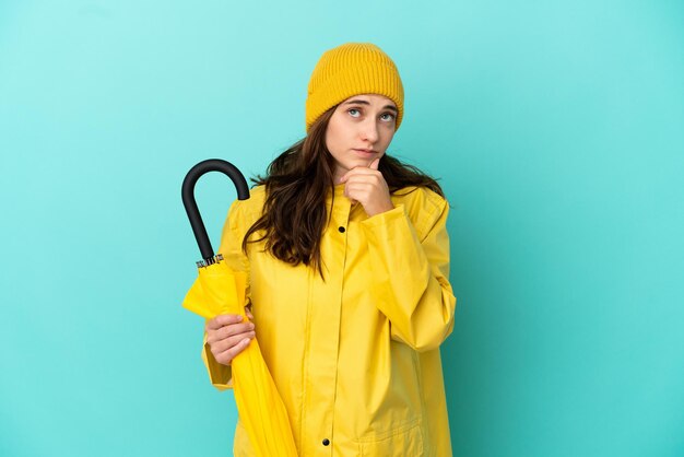 Jeune homme de race blanche tenant un parapluie isolé sur fond bleu ayant des doutes