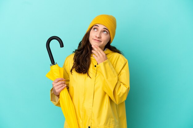 Jeune homme de race blanche tenant un parapluie isolé sur fond bleu en levant tout en souriant