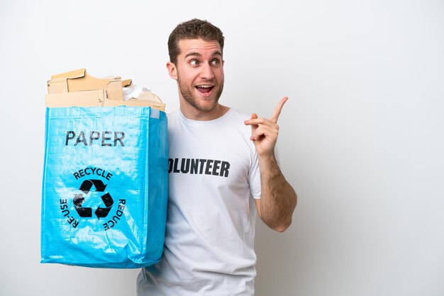 Jeune homme de race blanche tenant un sac de recyclage plein de papier à recycler isolé sur fond blanc dans l'intention de réaliser la solution tout en soulevant un doigt