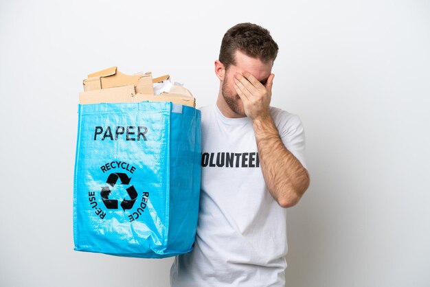 Jeune homme de race blanche tenant un sac de recyclage plein de papier à recycler isolé sur fond blanc avec une expression fatiguée et malade