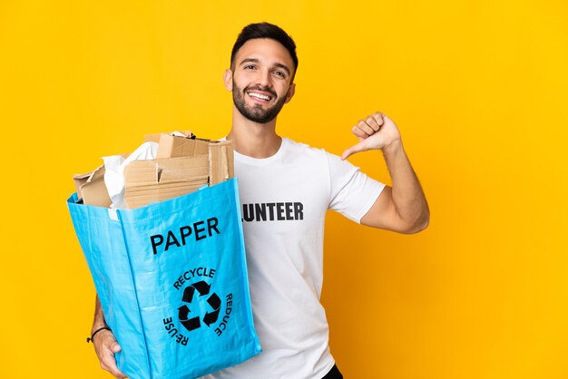 Jeune homme de race blanche tenant un sac de recyclage plein de papier à recycler isolé sur un mur blanc fier et satisfait de soi