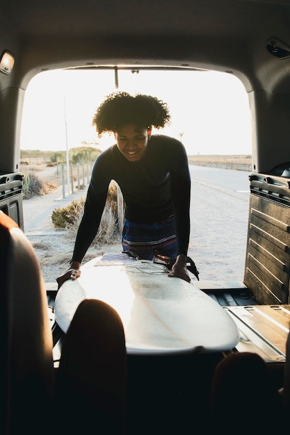 Photo jeune homme de race mixte attraper une planche de surf en caravane