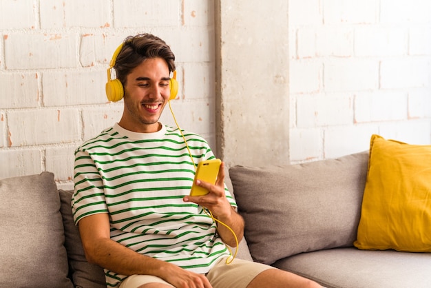 Jeune homme de race mixte écoutant de la musique assis sur le canapé