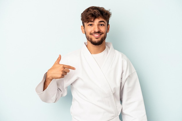 Jeune homme de race mixte faisant du karaté isolé sur fond bleu personne pointant à la main vers un espace de copie de chemise, fier et confiant