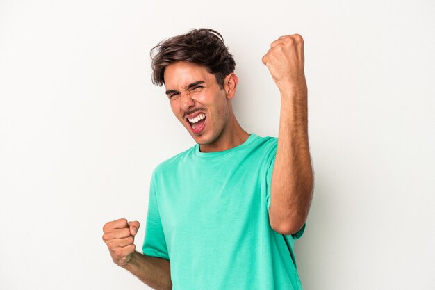 Jeune homme de race mixte isolé sur fond blanc acclamant insouciant et excité. Notion de victoire.