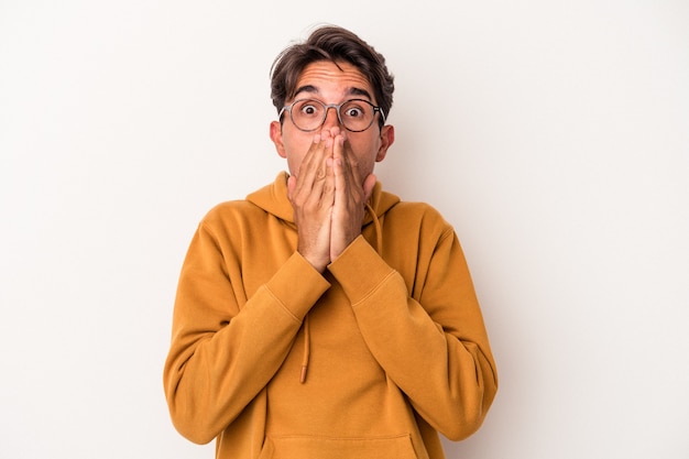 Jeune homme de race mixte isolé sur fond blanc choqué couvrant la bouche avec les mains.