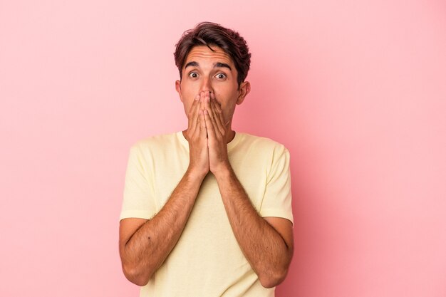 Jeune homme de race mixte isolé sur fond blanc couvrant la bouche avec les mains à l'air inquiet.