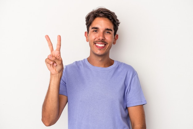 Jeune homme de race mixte isolé sur fond blanc joyeux et insouciant montrant un symbole de paix avec les doigts.