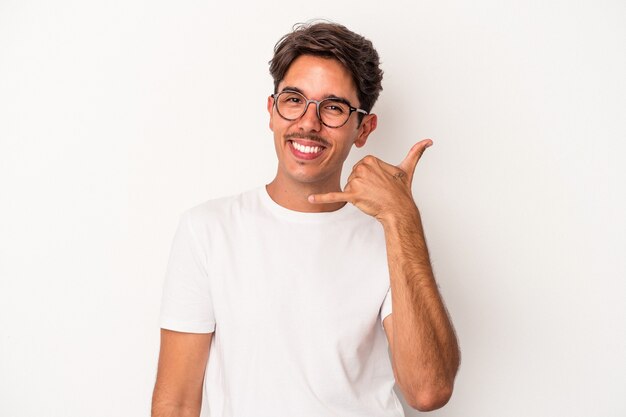 Jeune homme de race mixte isolé sur fond blanc montrant un geste d'appel de téléphone portable avec les doigts.