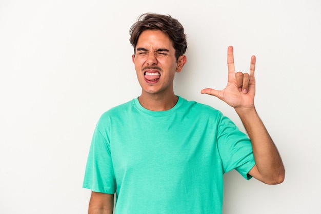 Jeune homme de race mixte isolé sur fond blanc montrant rock geste avec les doigts