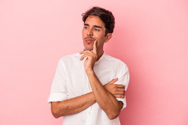 Jeune homme de race mixte isolé sur fond blanc regardant de côté avec une expression douteuse et sceptique.