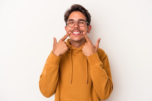 Jeune homme de race mixte isolé sur fond blanc sourit, pointant du doigt la bouche.