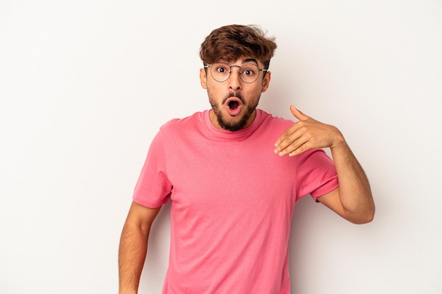 Jeune homme de race mixte isolé sur fond gris en riant de quelque chose, couvrant la bouche avec les mains.