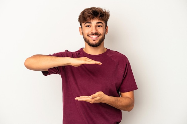 Jeune homme de race mixte isolé sur fond gris tenant quelque chose avec les deux mains, présentation du produit.