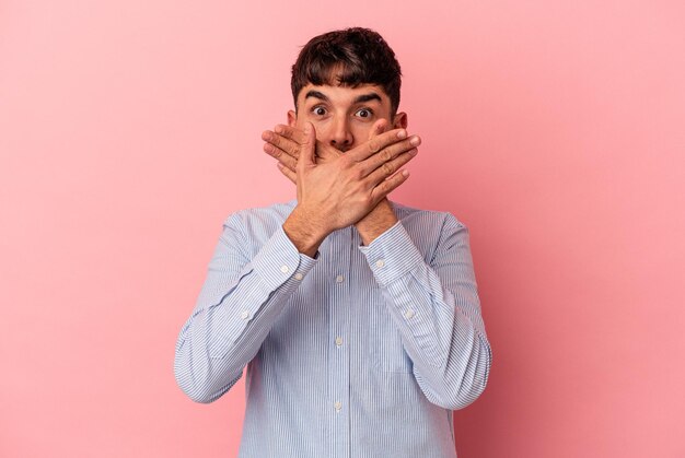 Jeune homme de race mixte isolé sur fond rose choqué couvrant la bouche avec les mains.