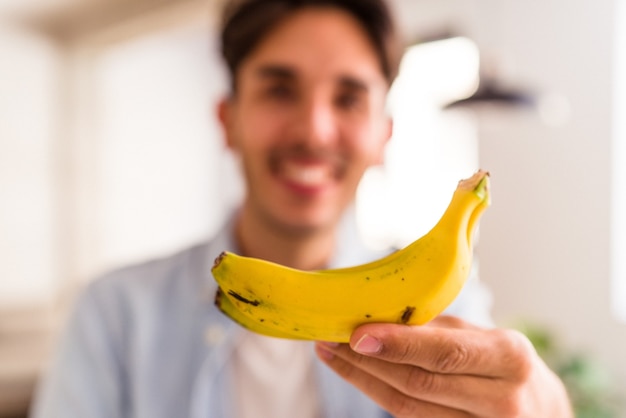 Jeune homme de race mixte mangeant une banane dans une cuisine de sa maison