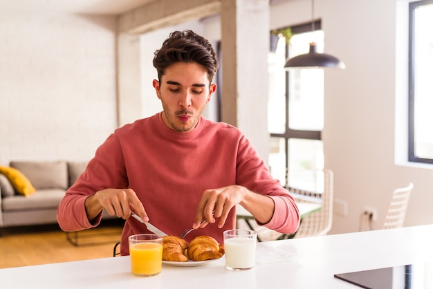 Jeune homme de race mixte mangeant un croissant dans une cuisine le matin