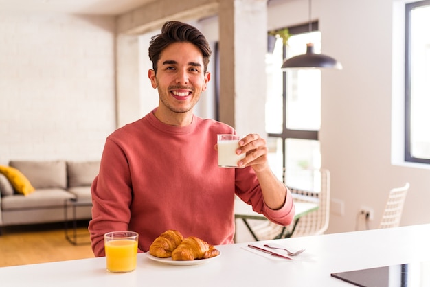 Jeune homme de race mixte mangeant un croissant dans une cuisine le matin