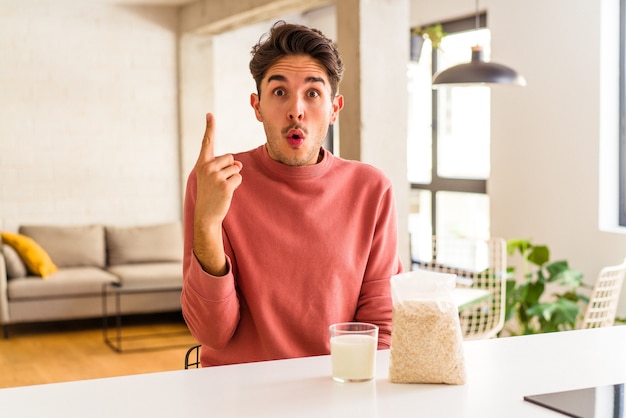 Jeune homme de race mixte mangeant de la farine d'avoine et du lait pour le petit déjeuner dans sa cuisine ayant une bonne idée, concept de créativité.