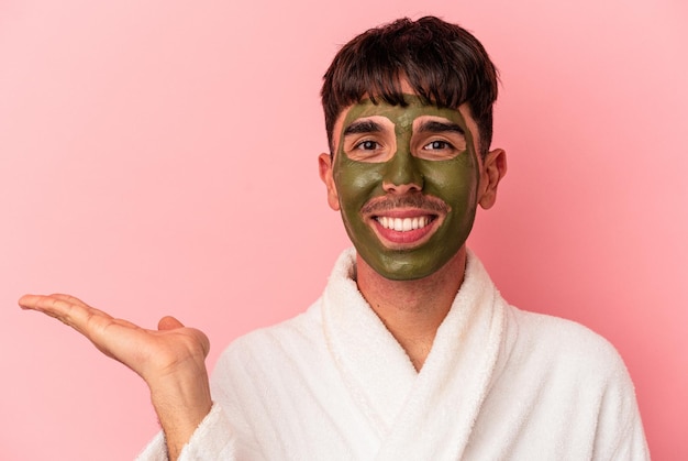 Jeune homme de race mixte portant un masque facial de beauté isolé sur fond rose