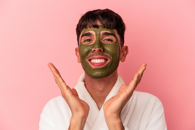 Jeune homme de race mixte portant un masque facial de beauté isolé sur fond rose