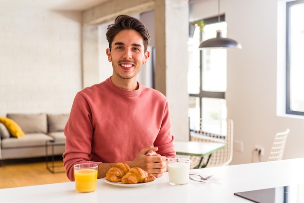 Jeune homme de race mixte prenant son petit déjeuner dans une cuisine le matin heureux, souriant et joyeux.