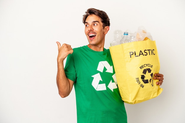 Jeune homme de race mixte recyclant du plastique isolé sur des points de fond jaune avec le pouce loin, riant et insouciant.