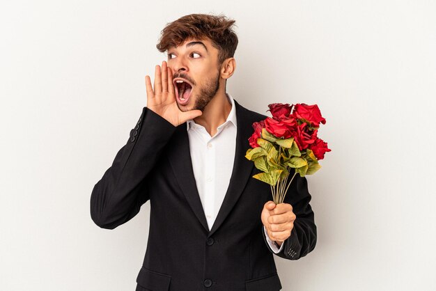 Jeune homme de race mixte tenant un bouquet de roses isolé sur fond blanc criant et tenant la paume près de la bouche ouverte.