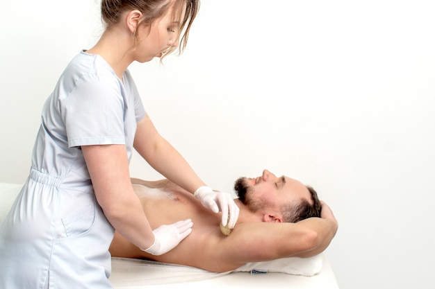 Jeune homme recevant l'épilation aisselle ou aisselle d'épilation par une jeune cosmétologue féminine dans un salon de beauté