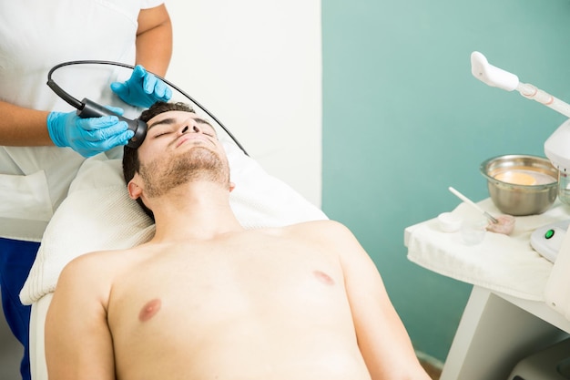 Jeune homme recevant un traitement facial anti-âge lors d'une visite dans une clinique de bien-être et un spa