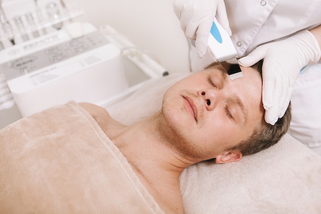 Jeune homme recevant un traitement de soin du visage par un cosmétologue