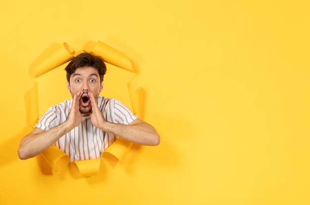 Jeune homme à la recherche et debout sur papier jaune déchiré fond vente intérieur type facial