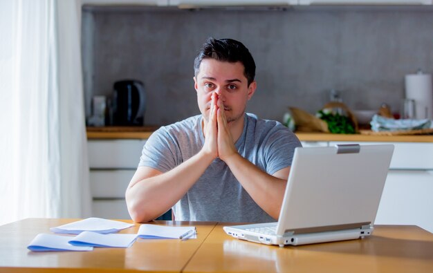 Jeune homme à la recherche d'un emploi dans Internet alors qu'il était assis à la cuisine avec un ordinateur portable.