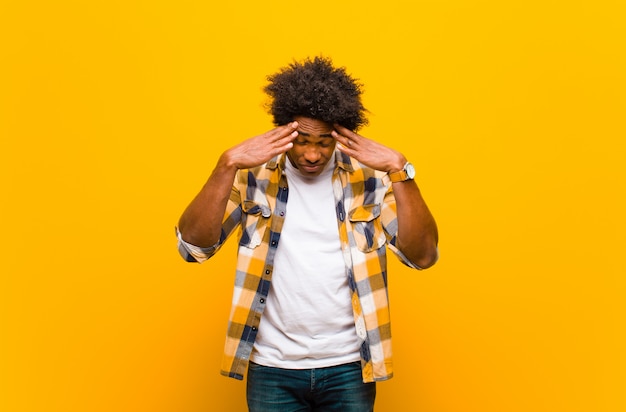 Jeune homme à la recherche de stress et de frustration, travaillant sous pression avec un mal de tête et troublé de problèmes sur le mur orange