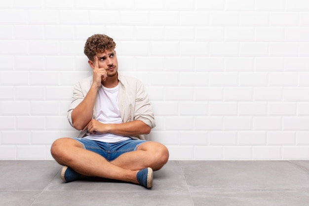 Jeune homme avec un regard concentré, se demandant avec une expression douteuse, regardant vers le haut et sur le côté