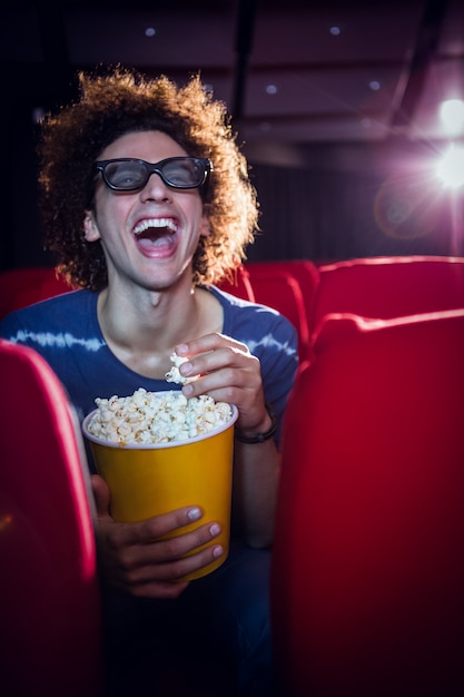 Jeune homme regardant un film 3d et manger du maïs soufflé