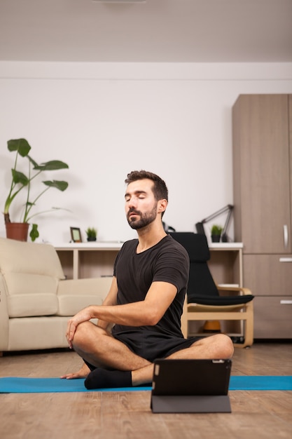 Jeune homme regardant le match alors qu'il s'étire le dos sur le sol. Entraînement de fitness