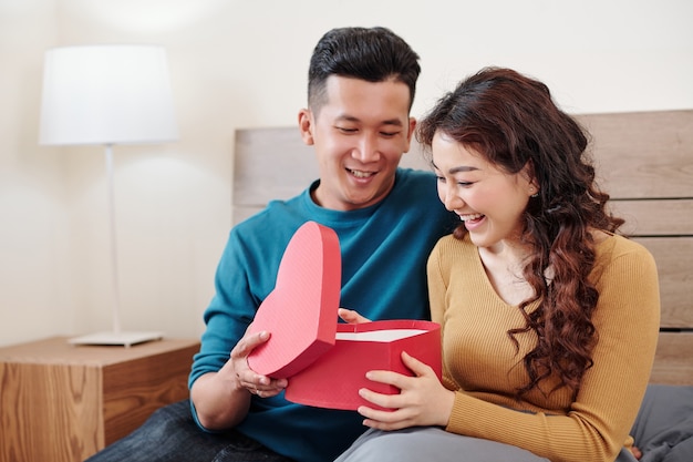 Jeune homme regardant la réaction de sa petite amie ouvrant le cadeau pour la Saint-Valentin