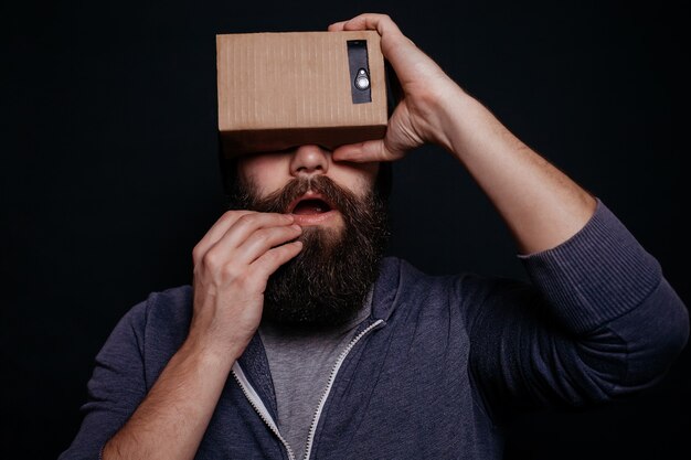 Jeune homme regardant à travers un casque VR en carton