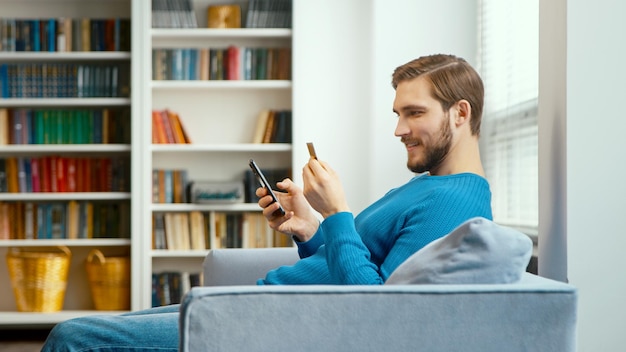 Le jeune homme regarde la carte bancaire en main et entre les chiffres sur le smartphone